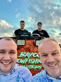 Group of anglers posing in front of the 'Bayou Bowfishing Charters' boat, showcasing a vibrant backdrop and camaraderie before their fishing adventure.
