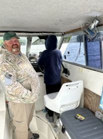 A fishing charter interior featuring a captain and a young angler at the helm, navigating through scenic waters.