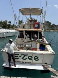 Two anglers proudly displaying a large Mahi-Mahi aboard the E-Zee charter boat in Montego Bay, Jamaica, with a scenic marina backdrop.