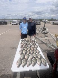 A group of anglers proudly displaying a large catch of Crappie on a table at a fishing spot, showcasing their successful day on the water.