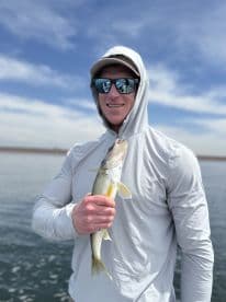 Angler proudly displaying a Walleye while fishing on a serene lake, showcasing a beautiful day outdoors.