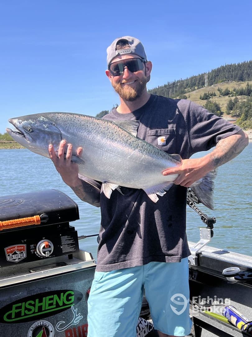 An angler proudly displaying a large Chinook Salmon while fishing on a scenic river, showcasing a successful day on the water.