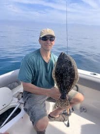 An angler proudly displaying a large Flounder while fishing on a calm day in open waters.