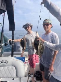 Two anglers proudly displaying their catch of Flounder while fishing on a boat in open waters.