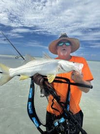 An angler proudly displaying a large Snook while standing in shallow water, showcasing a vibrant fishing environment.