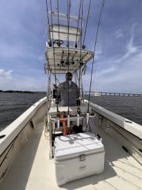 Interior view of a fishing boat showcasing the helm and seating area, with multiple fishing rods mounted and a cooler on board.