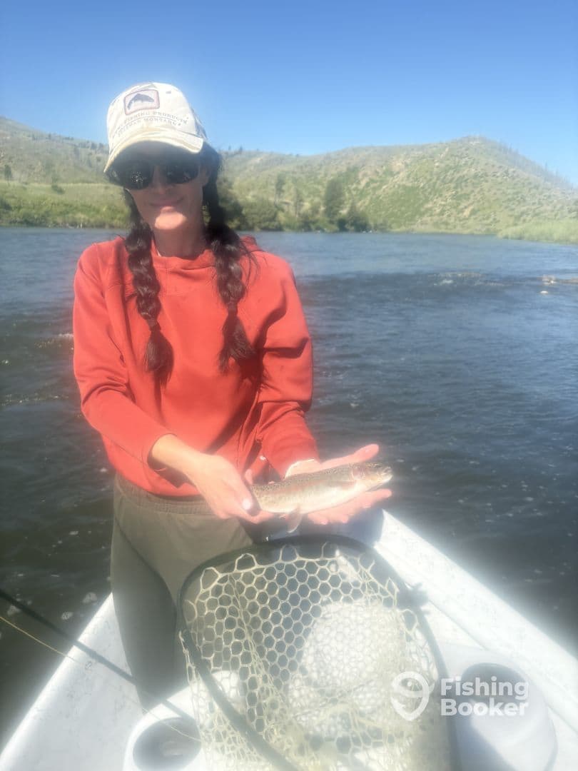 An angler proudly displaying a freshly caught trout while fishing on a scenic river, surrounded by lush greenery.