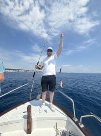 Angler actively reeling in a catch while fishing from a boat in clear blue waters, showcasing the excitement of the fishing experience.