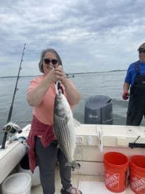 An angler proudly displaying a large Striped Bass while fishing on a boat, showcasing a successful day on the water.