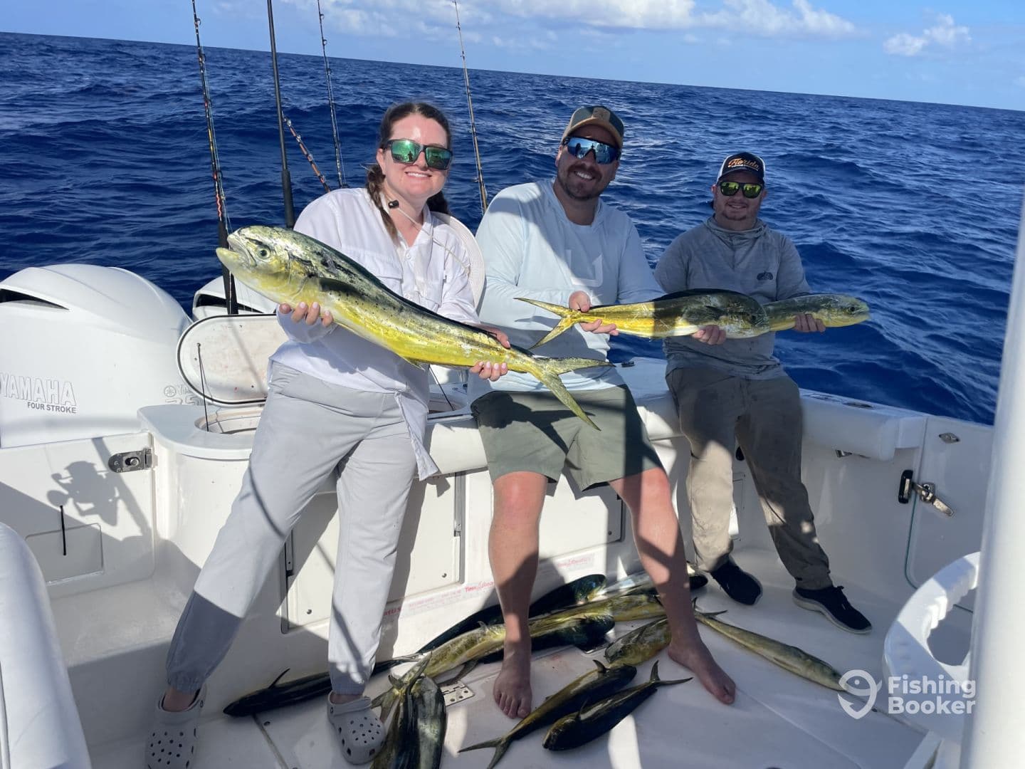 Three anglers proudly displaying their catch of Mahi Mahi aboard a fishing boat in open waters.