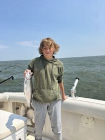 A young angler proudly displaying a caught fish while aboard a boat, enjoying a fishing trip on open waters.