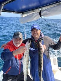 Two anglers proudly displaying their catch of Barracuda while fishing offshore, showcasing a successful day on the water.
