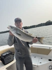 An angler proudly displaying a large Striped Bass while fishing on a boat, showcasing a successful day on the water.