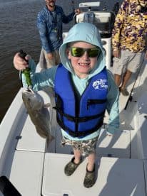 A young angler proudly displaying a caught fish while wearing a life jacket on a fishing boat.