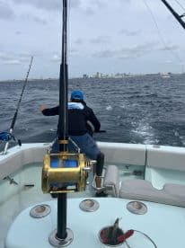 A young angler actively reeling in a fish while fishing from a center console boat, with a city skyline in the background.