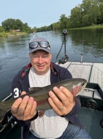 An angler proudly displaying a Rainbow Trout while fishing on a serene river, showcasing a successful catch during a relaxing day on the water.