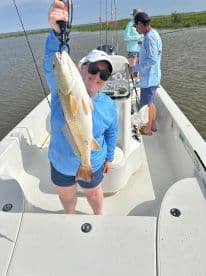 An angler proudly displaying a large Redfish while fishing on a charter boat in a scenic coastal environment.