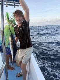 A young angler proudly displaying a fish while fishing on a boat, with a scenic ocean backdrop.