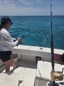 An angler actively reeling in a fish while fishing on a charter boat in clear blue waters.