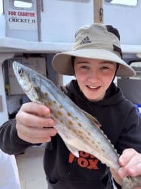 A young angler proudly displaying a speckled trout aboard the Cricket II charter boat, showcasing a successful fishing trip.