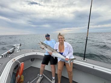 Two anglers proudly displaying a large King Mackerel on a boat during a fishing trip in open waters.
