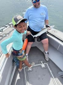 A young angler joyfully holding a fish while on a boat, accompanied by an adult, showcasing a fun fishing experience.