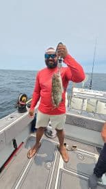 Angler proudly displaying a large Grouper while fishing on a charter boat in open waters.