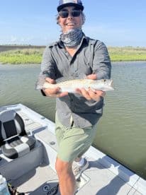 Angler proudly displaying a Speckled Trout while fishing on a boat in a coastal marsh environment.