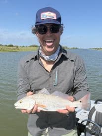Enthusiastic angler holding a Redfish while enjoying a sunny day on the water.