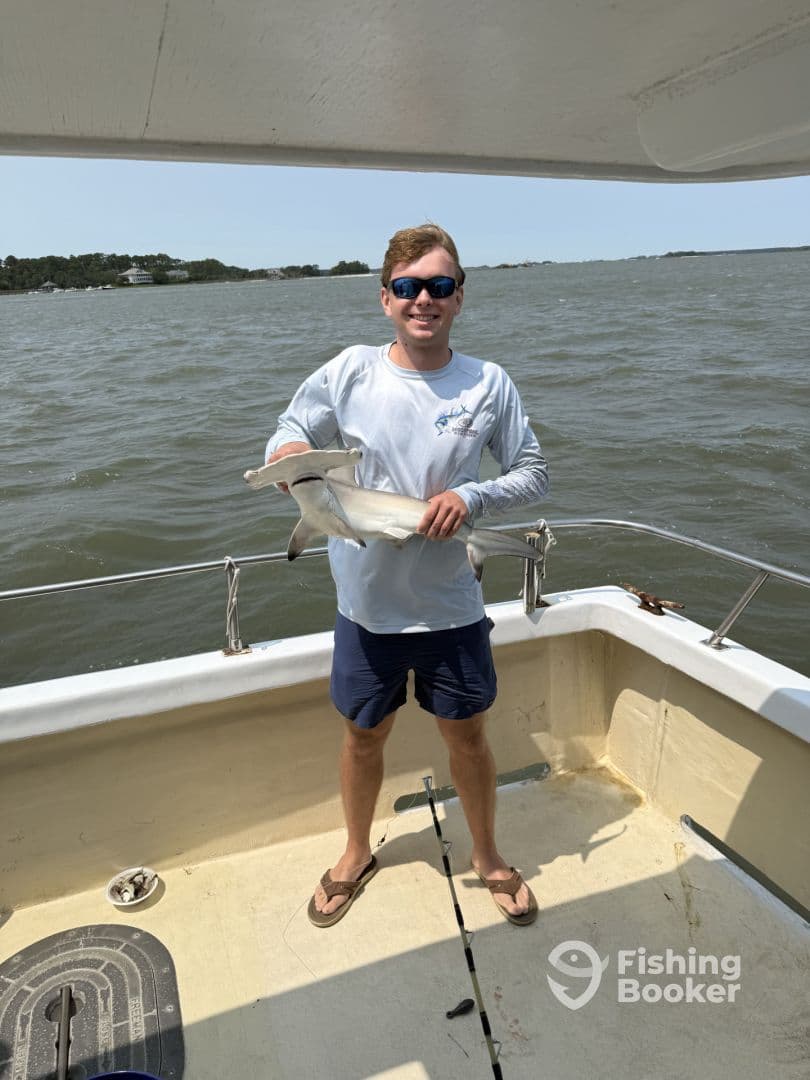 A young angler proudly displaying a caught shark on a boat during a fishing trip.