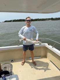 A young man proudly displaying a caught fish while aboard a boat, enjoying a sunny day on the water.