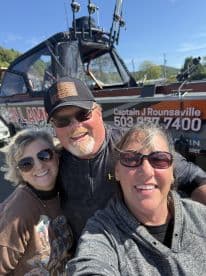 Three adults posing for a selfie in front of a fishing charter boat, showcasing the boat's exterior and fishing gear.
