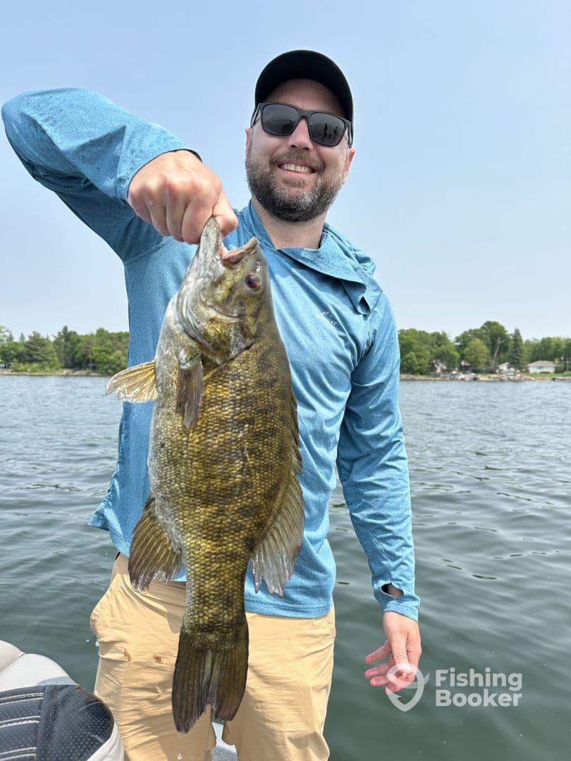 Angler proudly displaying a large Smallmouth Bass while fishing on a serene lake.