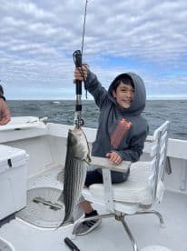 A young angler proudly displaying a striped bass while fishing on a boat, showcasing a fun day on the water.