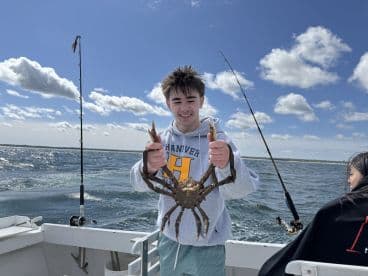A young angler proudly displaying a large crab while fishing on a boat, with a scenic backdrop of water and clouds.