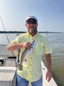 An angler proudly displaying a Speckled Trout while fishing from a boat in a calm coastal environment.