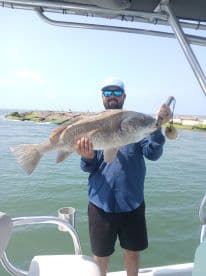Angler displaying a large Redfish while aboard a fishing boat, showcasing a successful day on the water.
