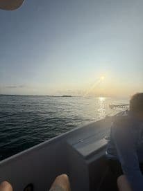 A serene sunset view from inside the boat, showcasing the calm waters and a passenger seated on the side.