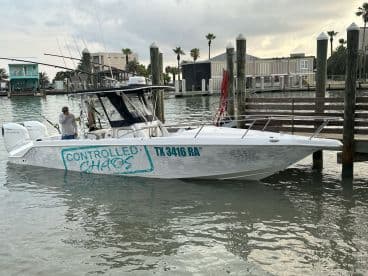 A sleek fishing boat named 'Controlled Chaos' docked in a calm marina, showcasing its modern design and fishing gear.