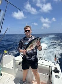 Young angler proudly holding a freshly caught fish while aboard a fishing boat in open waters.