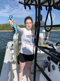 A young angler proudly displaying a Speckled Trout while fishing from a boat in a coastal environment.