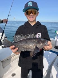 A young angler proudly displaying a Blackfish while fishing on a sunny day.
