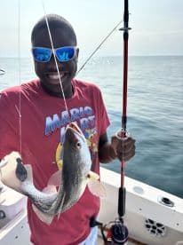 Young angler proudly holding a freshly caught fish while fishing on a boat, showcasing a fun day on the water.