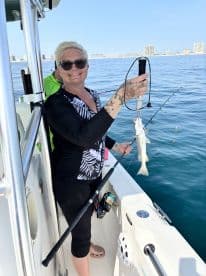 An angler proudly displaying a caught fish while fishing from a boat in clear waters, showcasing a vibrant fishing environment.