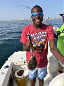 A young angler proudly displaying a caught Flounder while fishing on a boat, with a scenic coastal backdrop.