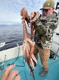 An angler proudly displaying a large octopus caught during a fishing trip in open waters.