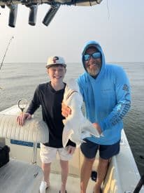 A young angler and an adult proudly displaying a caught shark while fishing on a boat, showcasing a memorable fishing experience.