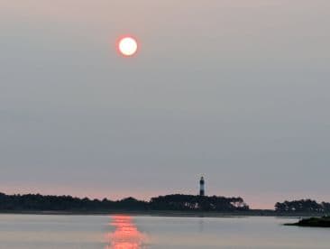 A serene sunset over the water, featuring a lighthouse in the distance, creating a tranquil fishing environment.