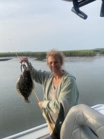 An angler proudly displaying a Flounder caught while fishing from a boat in a coastal marsh environment.