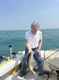 An older angler proudly displaying a Walleye while fishing on a sunny day, showcasing the excitement of a successful catch.